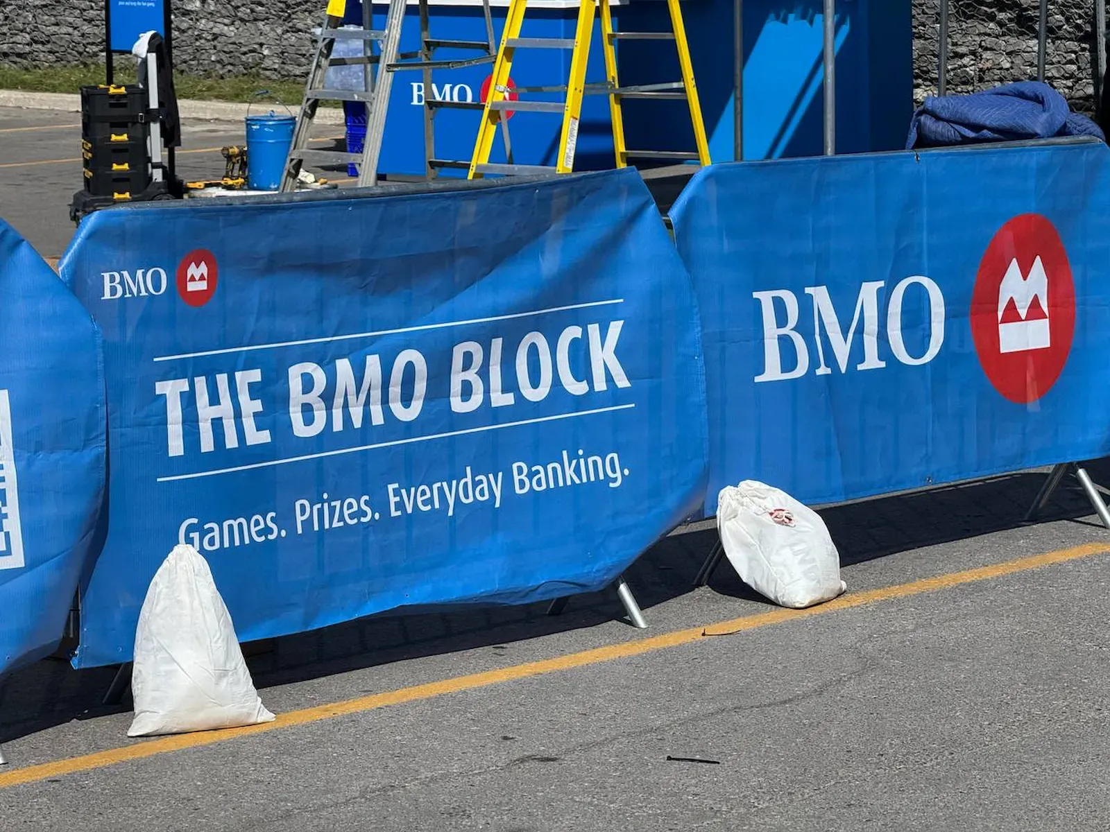 Bike rack barricade sections dressed in printed scrim covers, weighted with sandbags along a closed street